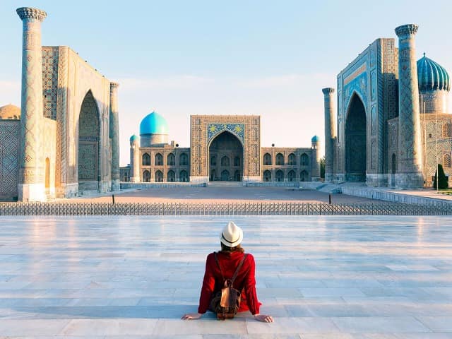 Tourist woman with hat and dress red sitting on registan an old public square uzbekistan