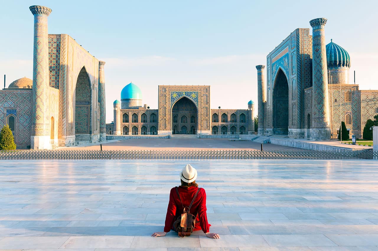 Tourist woman with hat and dress red sitting on registan an old public square uzbekistan