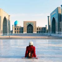 Tourist woman with hat and dress red sitting on registan an old public square uzbekistan
