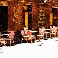 Wooden parisian coffee house with it s sidewalk tables and chairs in winter with the snow falling